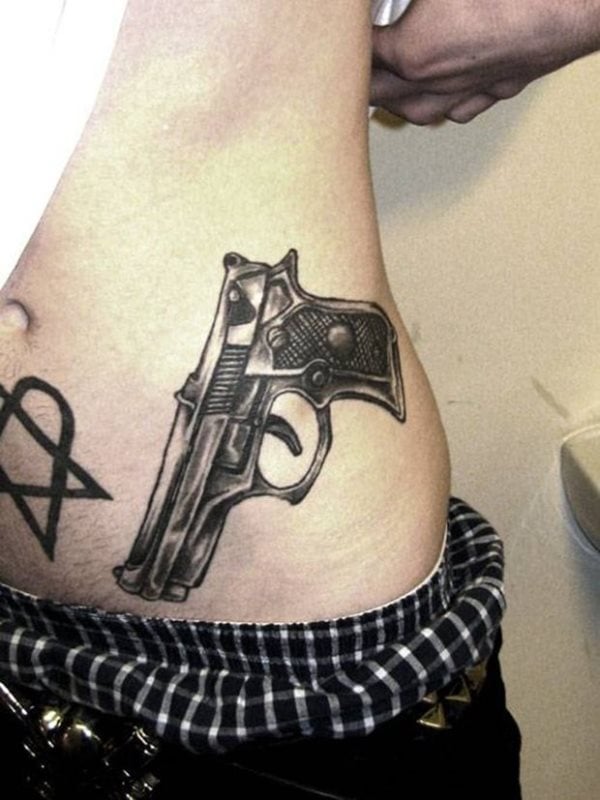 Tatuaje de una pistola sobre el costado, un tatuaje muy común y que ya hemos visto bastantes a lo largo de toda esta galería, por lo que si es tu idea, ya sabes que habrá muchas personas con un tatuaje similar