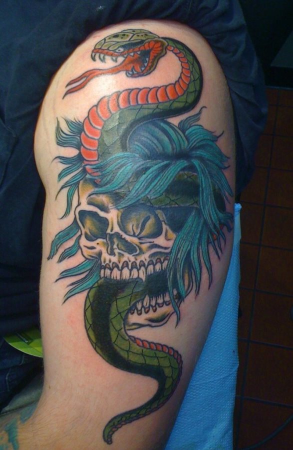 Tatuaje de una calavera con pelo azul y una serpiente naranja y verde sobre la cabeza