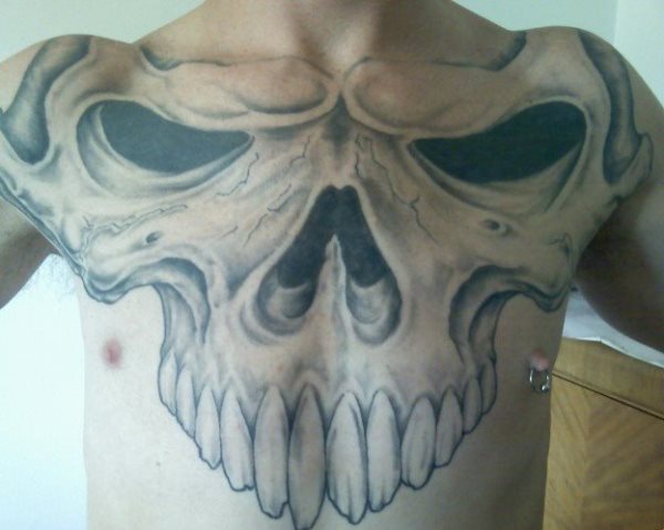 Tatuaje de una parte de la calavera, pero para la que se ha utilizado todo el pecho y los hombros y donde los grandes dietnes tatuados ocupan una gran parte del abdomen, además se ha adornado con un piercing en el pezón