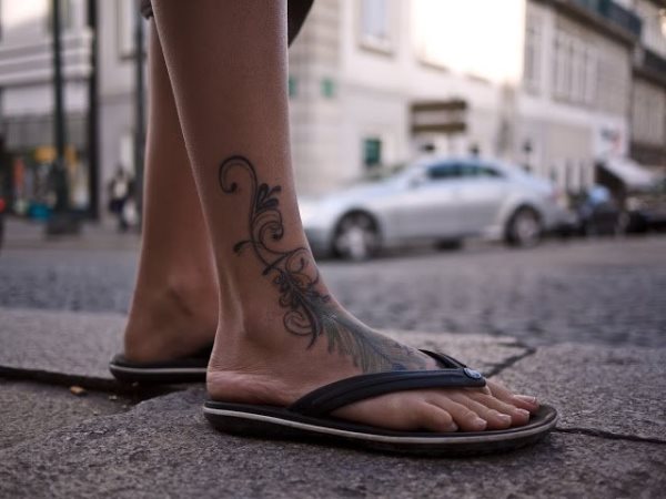 Tatuaje de pluma que empieza en el empeine y sigue subiendo en forma de enredadera de hojas por el tobillo hasta llegar a la espinilla, un tatuaje en que a pesar de sólo haberse utilizado el color negro lleva una carga muy grande de energía y alegría, un tatuaje que nos gusta mucho, ya que sin decir nada, expresa mucho sentido