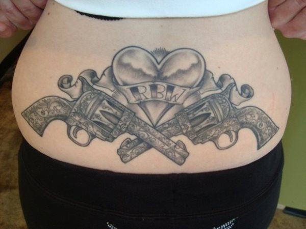 Tatuaje de dos pistolas en la espalda, ambos revolver se encuentran cruzados y tienen grandes gravados, además en el centro podemos ver un corazón con las iniciales RBW, tal vez el nombre de una persona muy querida para este tatuado