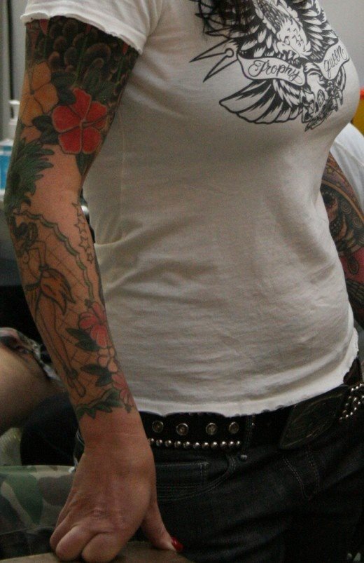 Brazo completamente tatuado el de esta chica que se ha basado en unos fondos oscuros y unas flores en tonos suaves que junto a la hawaiana que tiene tatuada bajo el codo hacen de este un tatuaje digno de admirar