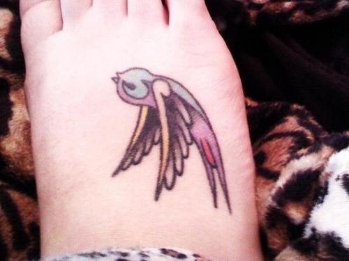 Tattoo en el empeine para el que se ha tatuado una pequeña golondrina con alas negras y remates en amarillo