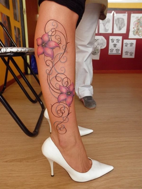 Tatuaje de unas pequeñas flores de estilo hawaiano a color lila, rodeadas por unas cenefas negras y turquesas, que llaman especialmente la atención por los trazos tan finos conseguidos, tal vez el detalle que más nos guste del tattoo