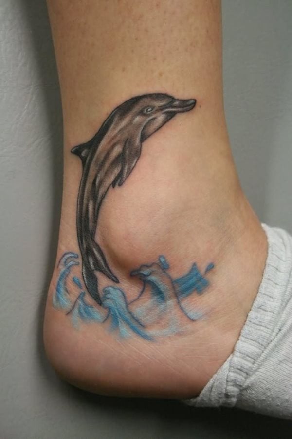 Un sencillo delfín que salta sobre el mar situado el delfín sobre el tobillo y las olas celestes sobre el empeine dan como resultado un trabajo excelente por parte del tatuador y un gusto exquisito por parte del tatuado