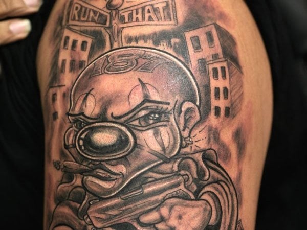 Payaso enfadado y con pistola con un fondo de ciudades que dan un toque gangster a este tatuaje en el que nos llama la atención el número 187 tatuado en a cabeza del propio tattoo, ya que creemos que es una peculiar idea la de tatuar algo al propio tatuaje