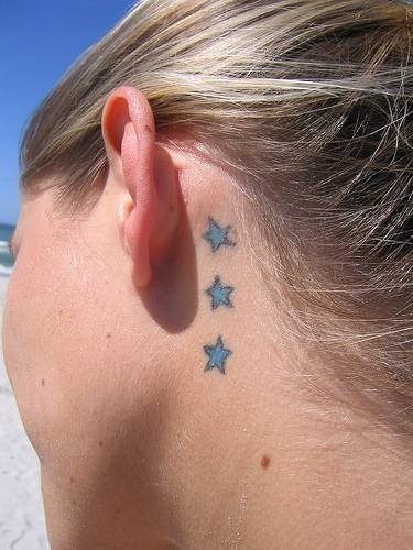 Imagen de un tatuaje de tres estrellas azules tras la oreja