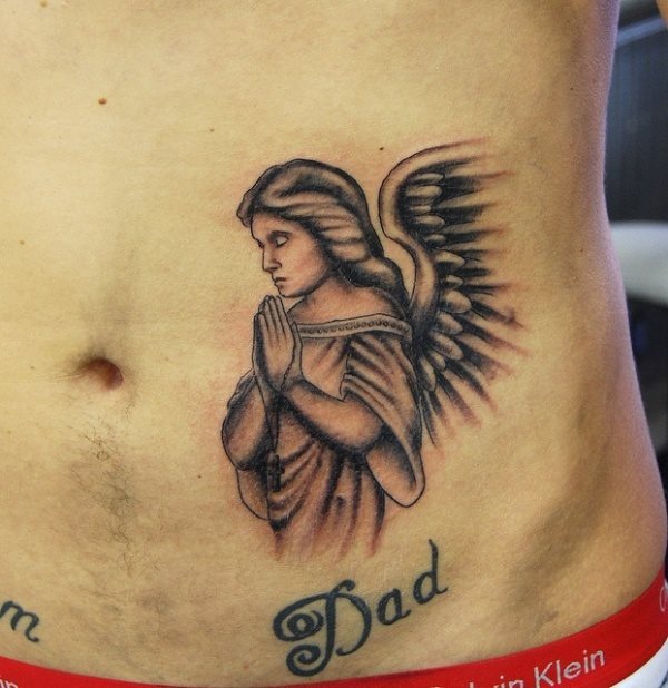 Tatauje de un ángel rezando sobre la palabra dad, una bonita idea para aquellos a los qu esu padre no les acompañe ya en esta vida o que en vez de poner Dios han puesto su sinónimo, el de Padre y se han hecho este tatuaje para que les conceda todas las súplicas de sus oraciones