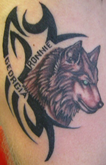 Tatuaje de un lobo rodeador por un tribal y un par de nombres, un tatuaje seguro que con mucho significado para la persona que lo lleva, pero que a nosotros no nos dice demasiado, aún así es un buen trabajo y queda bien por su tamaño pequeño