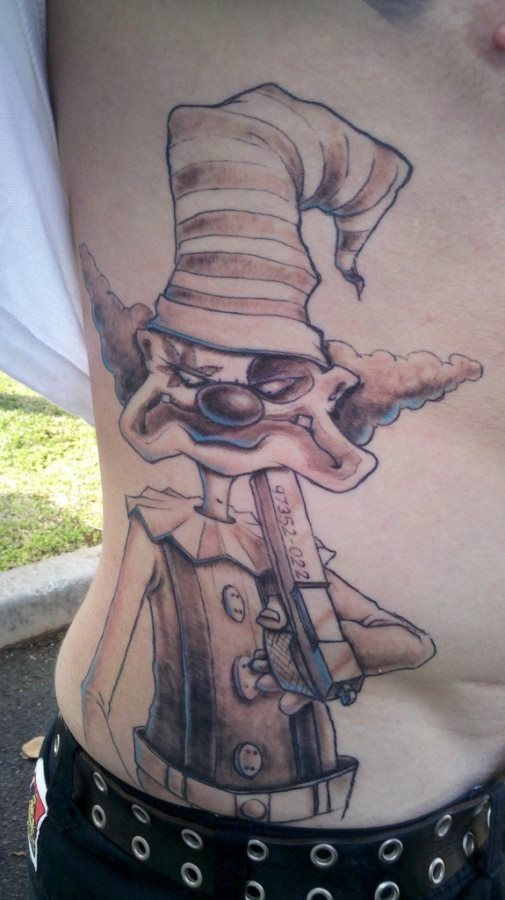 Tattoo en el costado de un payaso que por muy enfadado que quiera parecer nos parece muy simpático, con ese pelo tan típico de los payasos y el gorro torcido, destaca la originalidad del maquillaje del payaso en un ojo y la pistola que esperemos esté usando para rascarse y no para pegarse un tiro, sería una pena