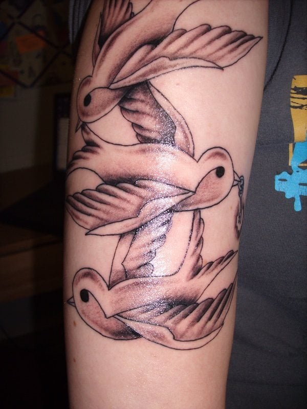Conjunto de tres golondrinas componen este tatuaje, todas las golondrinas están superpuestas unas encima de otras para hacer un precioso tatuaje de pájaros, en el que como podemos apreciar, la golondrina de en medio lleva algo sobre su pico, como una especie de pequeña cadenita