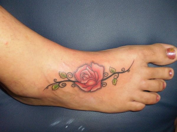 Tatuaje de una rosa roja sobre el pie para el que se han dibujado unas hojas pequeñas verdes y unos tallos curvos que le dan un toque distinguido a este tatuaje, dándole una forma muy plana sobre el pie
