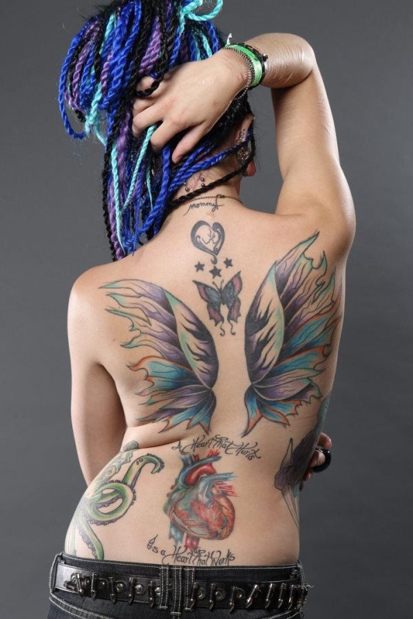 Composición de varios tatuajes sobre la espalda, donde podemos apreciar unas enormes y coloridas alas que es el tatauje de mayor tamaño, pero también hay otros tatuajes, como unas estrellas, una mariposa o el corazón relleno por una silueta de dos personas besándose