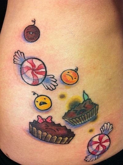 Simpático y origina ltatuaje de caramelos y chucherías, además de incluir unas simpáticas caras de colores, un tatuaje que nos ha encantado por la diversión y alegría que transmite, al igual que las magdalenas nos han encantado