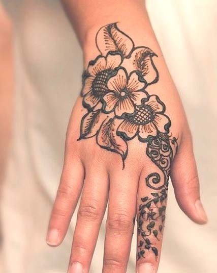 Espectacular y fijo tatuaje a color negro de varias flores con hojas en la mano, del cual lo que más nos gusta son las pequelas hojas que van rodeando a todo el dedo y que llegan casi hasta la uña