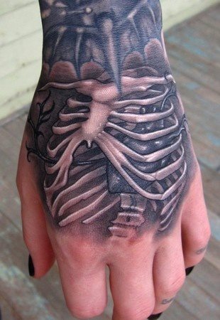 Huesos tatuados sobre la mano, que como podemos ver es el final a un gran tatuaje que viene recorriendo todo el brazo