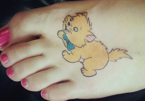 Divertido e infantil diseño de un pequeño gatito con un lazo azul en el cuello, tatuaje que ha sido colocado sobre el pie y que por su tamaño y su forma nos parece un tatauje muy acertado para una chica que no quiere un gran tatuaje y además quiere un tatauej que le transmita alegría