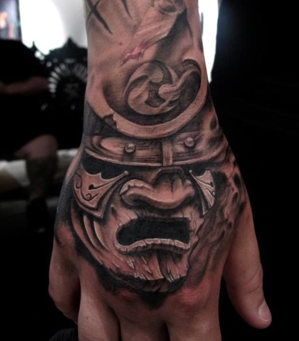 Gran tatuaje del casco de un guerrero sobre la mano hacen de este dibujo un gran tatuaje, en el que el tatuador se ha esmerado en conseguir unos grandes y buenos detalles, al igual que una cara muy expresiva, cuyos trazos dan un aire de madera al tatuaje que nos encanta