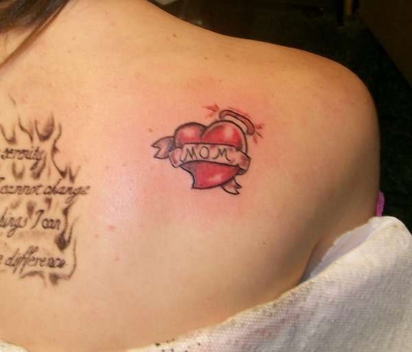 Pequeño corazón en la espalda, tatuado de color rojo y con una pequeña corona con destellos a un lado, en su interior se ha dejado la palabra mom tatuada para el resto de tu vida, como es el amor de una madre, infinito y para toda la vida